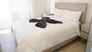 Una cama bien hecha con una colcha blanca y un edredón oscuro doblado al pie.