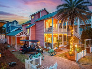 A multi-story building with balconies, a covered porch, and a driveway with bicycles and a golf cart.