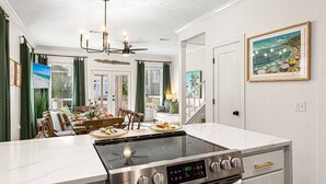 A modern kitchen with a stainless steel stove, white marble countertops, and a dining area with a table set for two. - 30A |15 sec walk to Private Beach | Htd pool | Bikes | Golf Cart | Gulf View (Santa Rosa Beach)