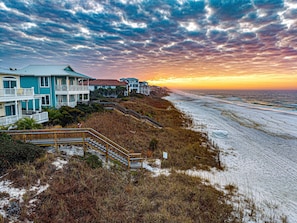 A beachfront property with multiple houses, a staircase leading to a beach, and a view of the ocean at sunset.