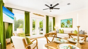 A room with a dining table set for four, a sofa, a ceiling fan, and a large window with green curtains. - 30A |15 sec walk to Private Beach | Htd pool | Bikes | Golf Cart | Gulf View (Santa Rosa Beach)