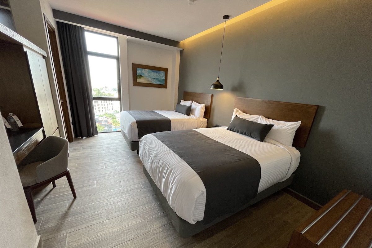 Een hotelkamer met twee bedden, een bureau en uitzicht op de omgeving.