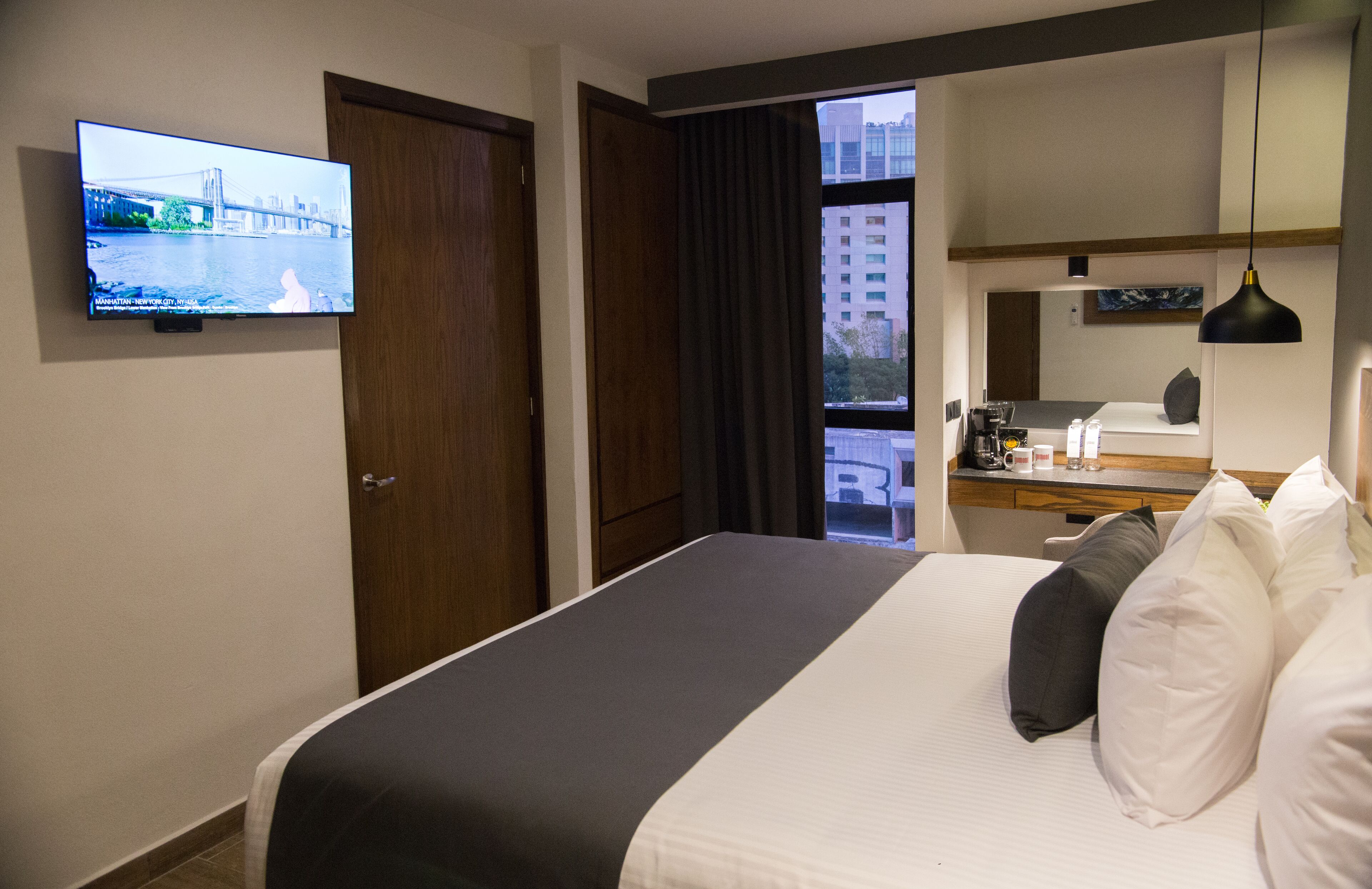 Hotelkamer met een bed, een aan de muur bevestigde televisie, een bureau met spiegel en een raam met uitzicht op gebouwen.