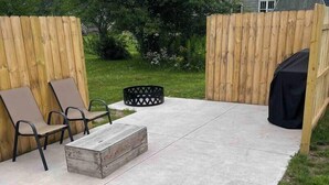 Un pati amb paviment de formigó, dues cadires de metall, una taula de fusta petita i una barbacoa negra.