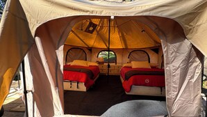 Una tienda de campaña con dos camas, cada una con ropa de cama y almohadas rojas, y una pequeña zona de estar.
