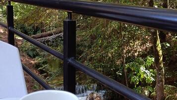 A white mug on a table with a railing overlooking a forested area.