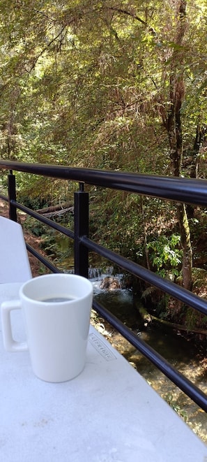 Una taza blanca sobre una mesa con barandilla, con vistas a una zona boscosa.