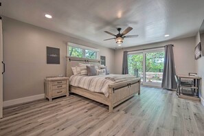 A bedroom with a wooden bed, a nightstand, a desk with a chair, and a large window with a view of greenery. - Airy Alpine Getaway w/ Lake Arrowhead Views! (Lake Arrowhead)