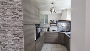 A modern kitchen with a stone wall, wooden cabinets, a stainless steel refrigerator, and a hanging light fixture. - Lovely house with private parking/covered terrace close to beaches and amenities. (Douarnenez)