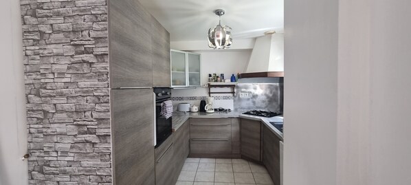 Eine moderne Küche mit Steinwand, Holzschränken, einem Edelstahlkühlschrank und einer Pendelleuchte.