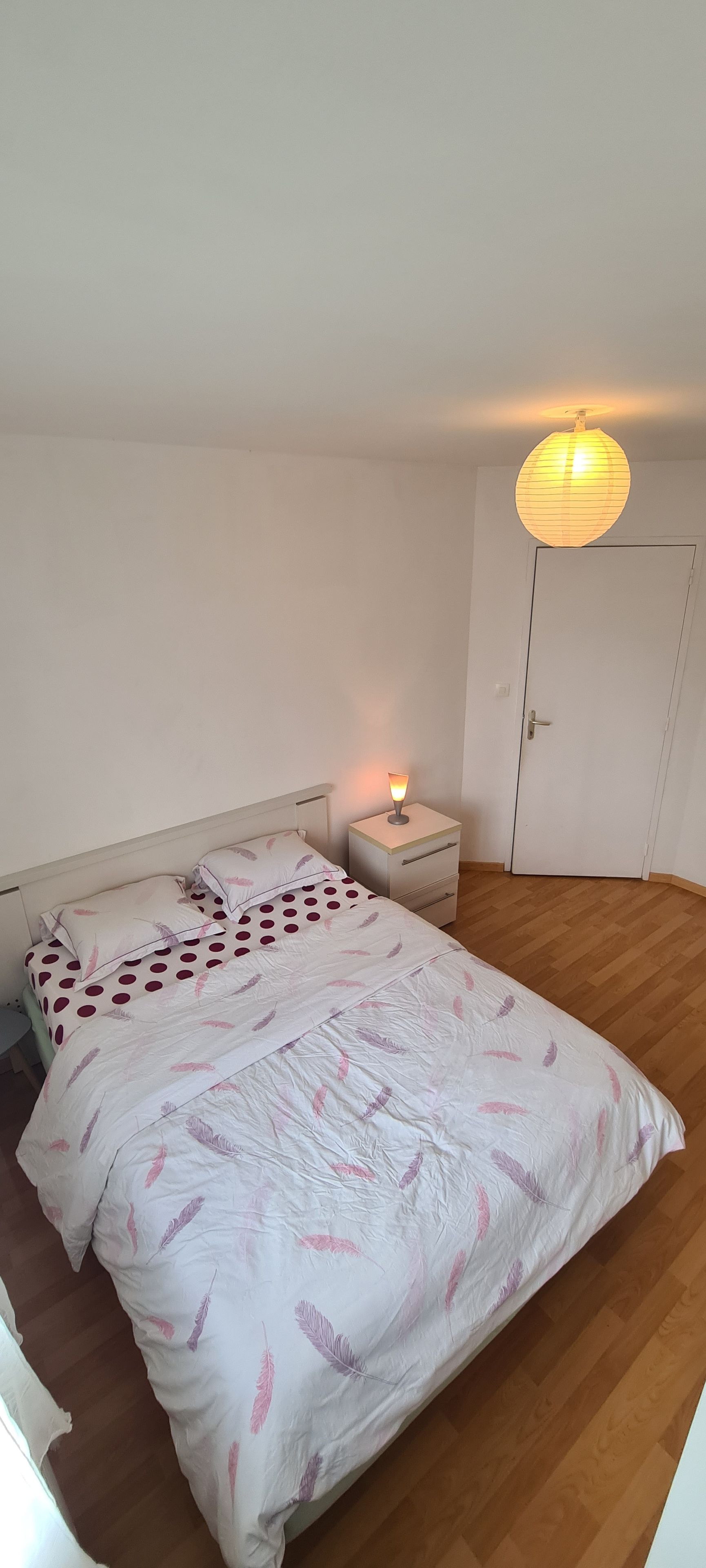 Ett sovrum med en säng, ett sängbord, en nattduksbord, en lampa och en dörr.