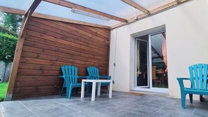 A covered patio with wooden walls, a sliding glass door, and blue plastic chairs and a table. - Lovely house with private parking/covered terrace close to beaches and amenities. (Douarnenez)