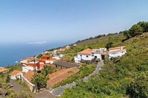 Uma vila costeira com edifícios brancos e telhados vermelhos, rodeada por vegetação e com vista para o mar.