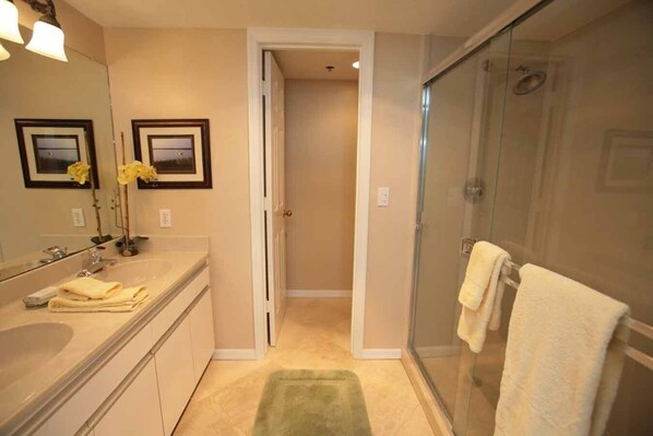 Une salle de bain avec une douche à parois de verre, un lavabo avec un miroir et une porte donnant sur une autre pièce.
