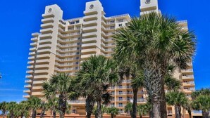 A multi-story hotel with balconies, palm trees in the foreground, and a clear blue sky. - Dazzling Dune Delight | Inlet #902 (New Smyrna Beach)