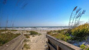 A wooden boardwalk leading to a beach with sand dunes and sea grass. - Dazzling Dune Delight | Inlet #902 (New Smyrna Beach)
