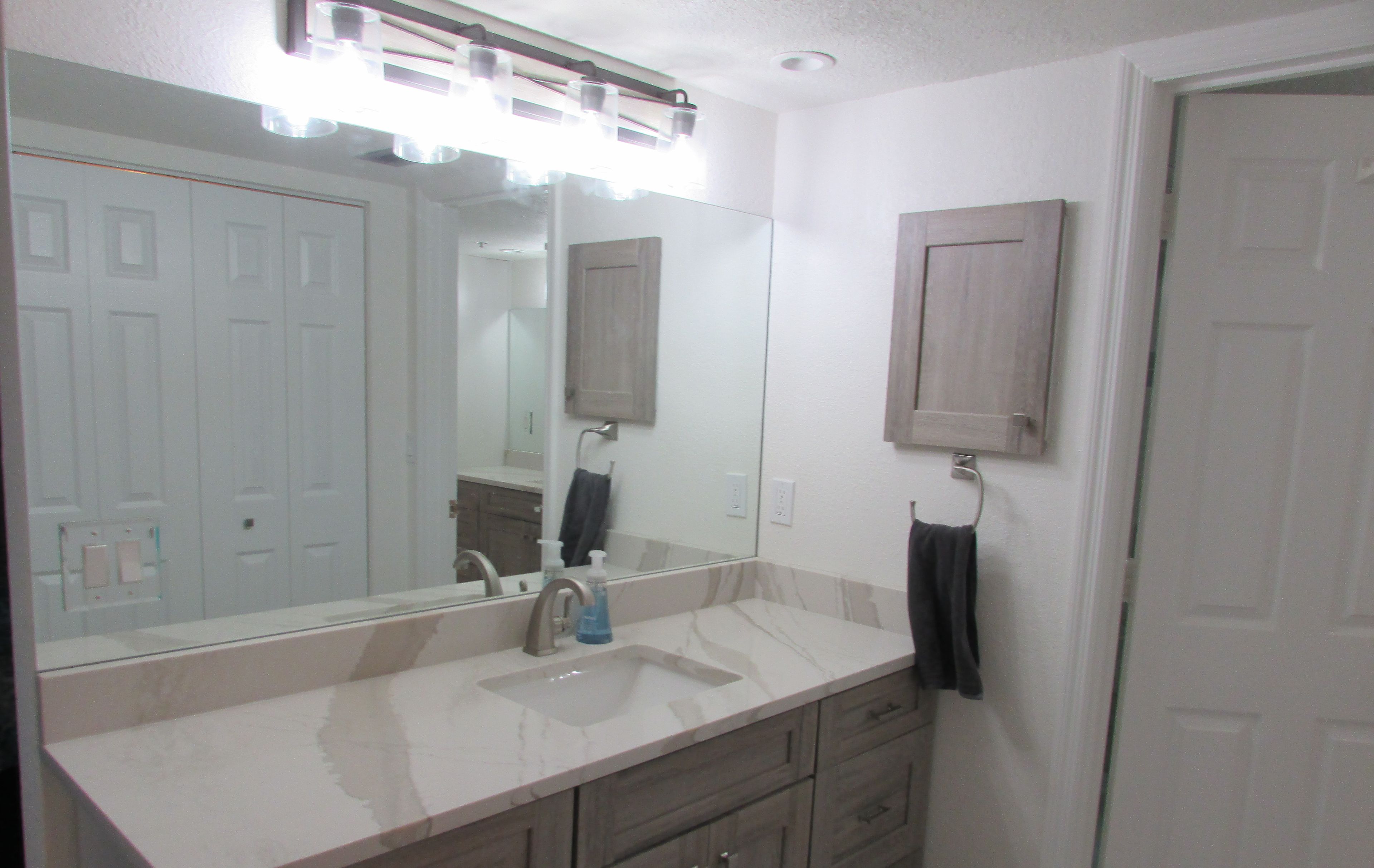 A bathroom with a large mirror, a sink, and wooden cabinets.