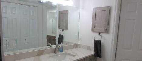 A bathroom with a large mirror, a sink, and wooden cabinets.