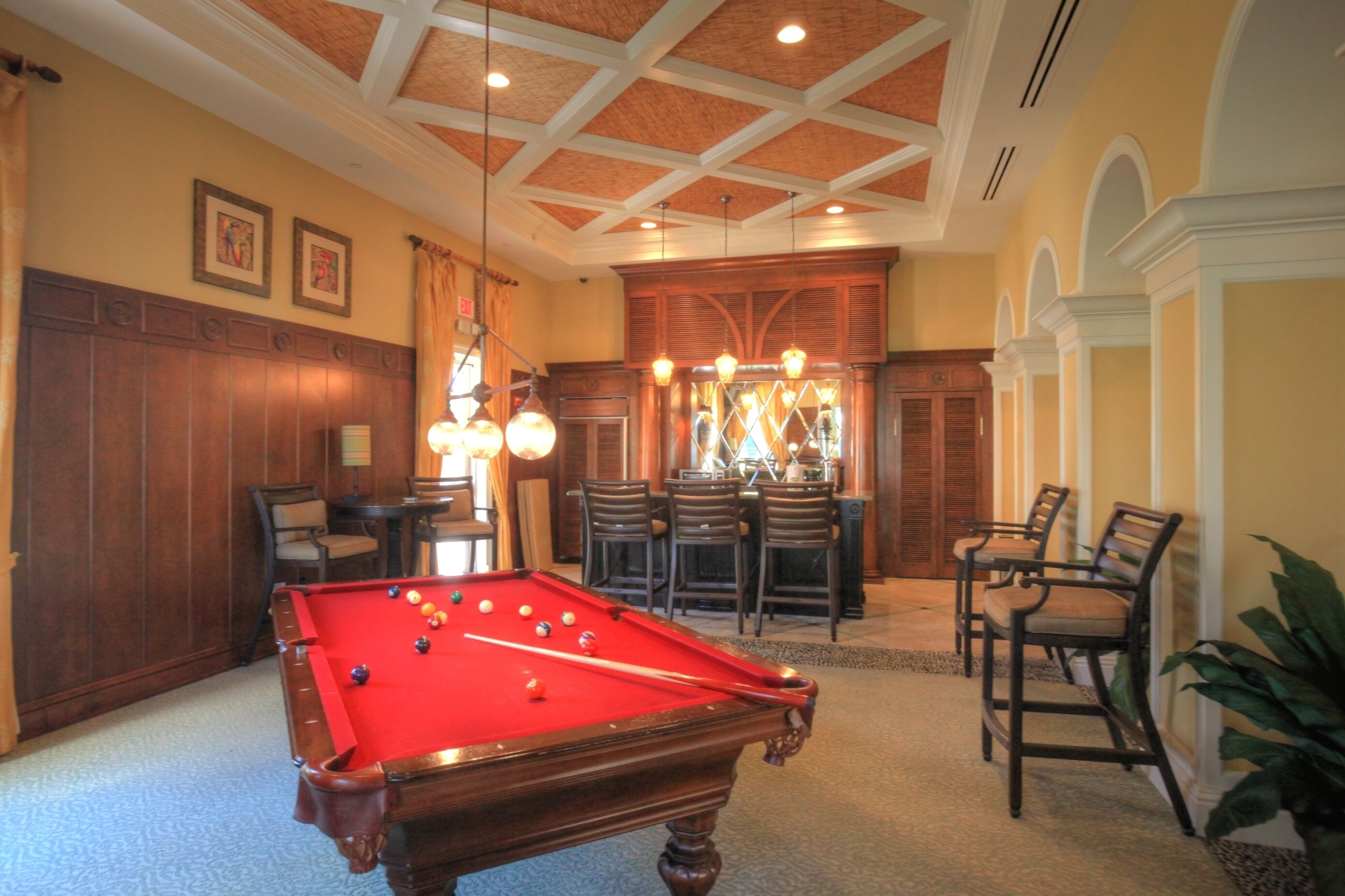 Une table de billard dans une pièce aux murs lambrissés, avec un coin bar et plusieurs chaises.
