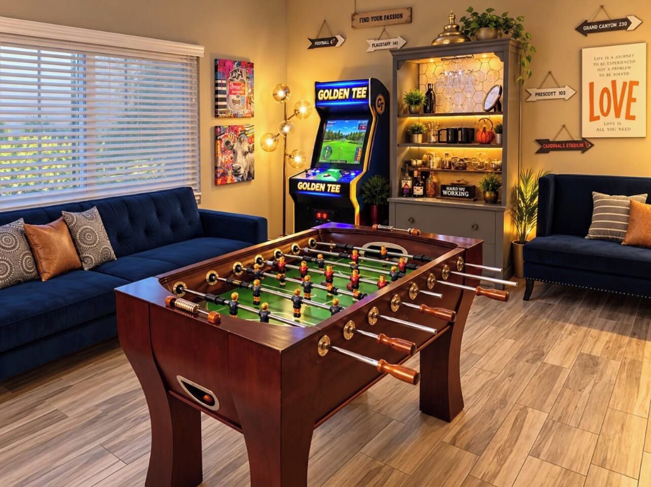 A room with a foosball table, a foosball table with a screen, and a bar area with shelves.