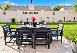 An outdoor patio with a table set for dining, chairs, and a decorative wall with the word 'ARIZONA' on it. - Luxury 3-Bedroom Home with Pool Near Stadium-Perfect for Game Weekends (Glendale)