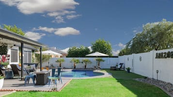 A backyard with a swimming pool, lounge chairs, and a covered patio area.