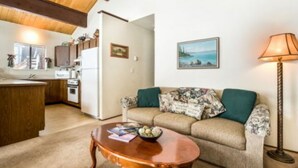 A cozy living room with a sofa, a coffee table, and a lamp. There is a kitchen area with cabinets and a refrigerator.