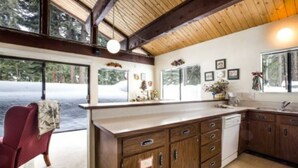 A kitchen with wooden cabinets, a white countertop, and a window overlooking a snowy landscape.