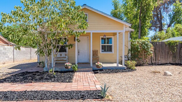A single-story house with a front porch, a small garden, and a wooden fence.