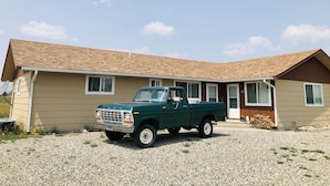 A green Ford truck parked in front of a beige house with a sloped roof. - Tidy Country Cottage 5 minutes outside of Cody (Cody)