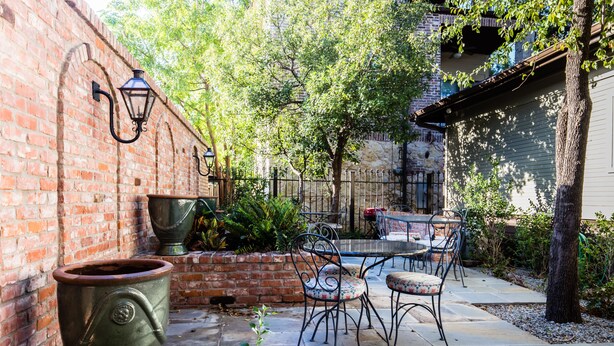 A patio with a brick wall, a metal table and chairs, and a large planter. - It's Our Location...Easy to get to many Dallas Destinations (Dallas)