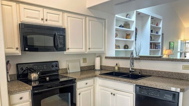 A kitchen with white cabinetry, a black microwave, a stove, a dishwasher, and a granite countertop.