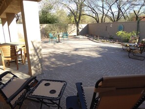 An outdoor patio area with seating arrangements, including chairs and a table, surrounded by a low wall and trees.