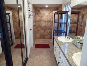 A bathroom with a walk-in shower, two sinks, a large mirror, and a tiled floor.