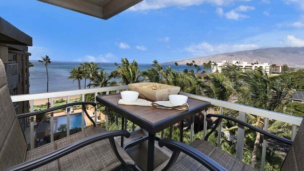 A balcony with a table set for two, overlooking a beach and ocean.