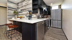 A modern kitchen with a central island, black cabinets, stainless steel appliances, and a wooden backsplash.