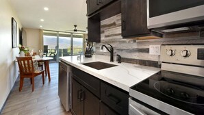 A modern kitchen with dark cabinets, a large island, stainless steel appliances, and a view to the outdoors.