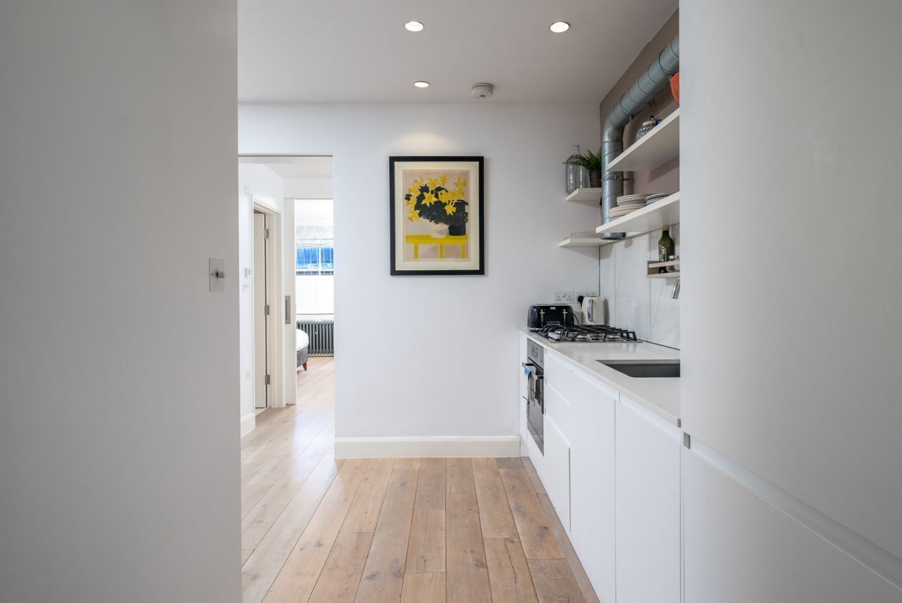 A modern kitchen with white cabinets, a gas stove, and a framed artwork on the wall.
