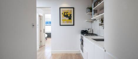 A modern kitchen with white cabinets, a gas stove, and a framed artwork on the wall.