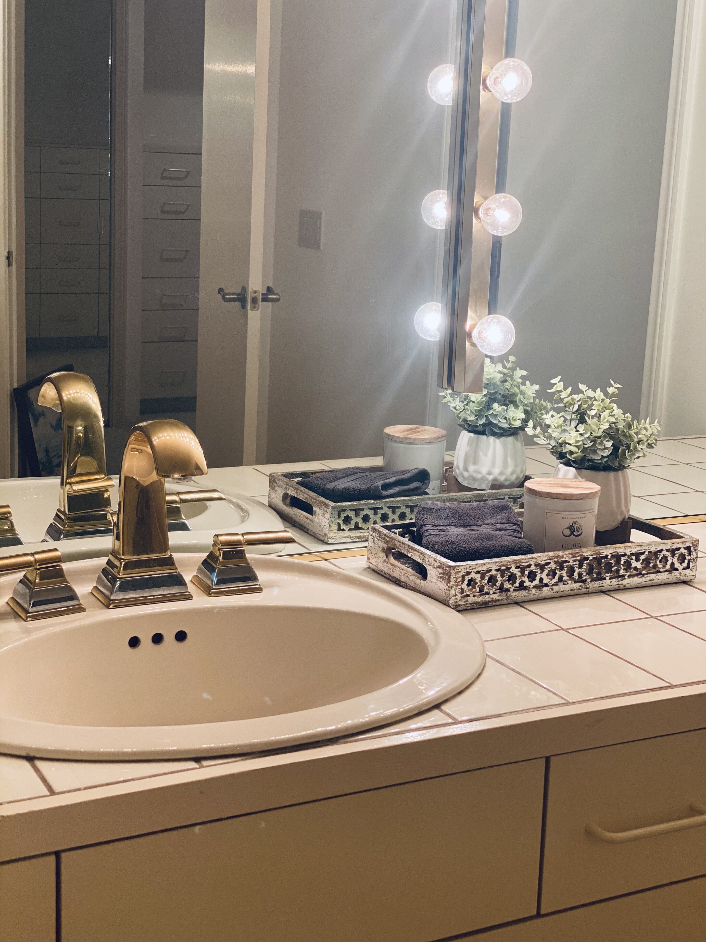 Un tocador de baño con un espejo grande, luces de tocador y un lavamanos.