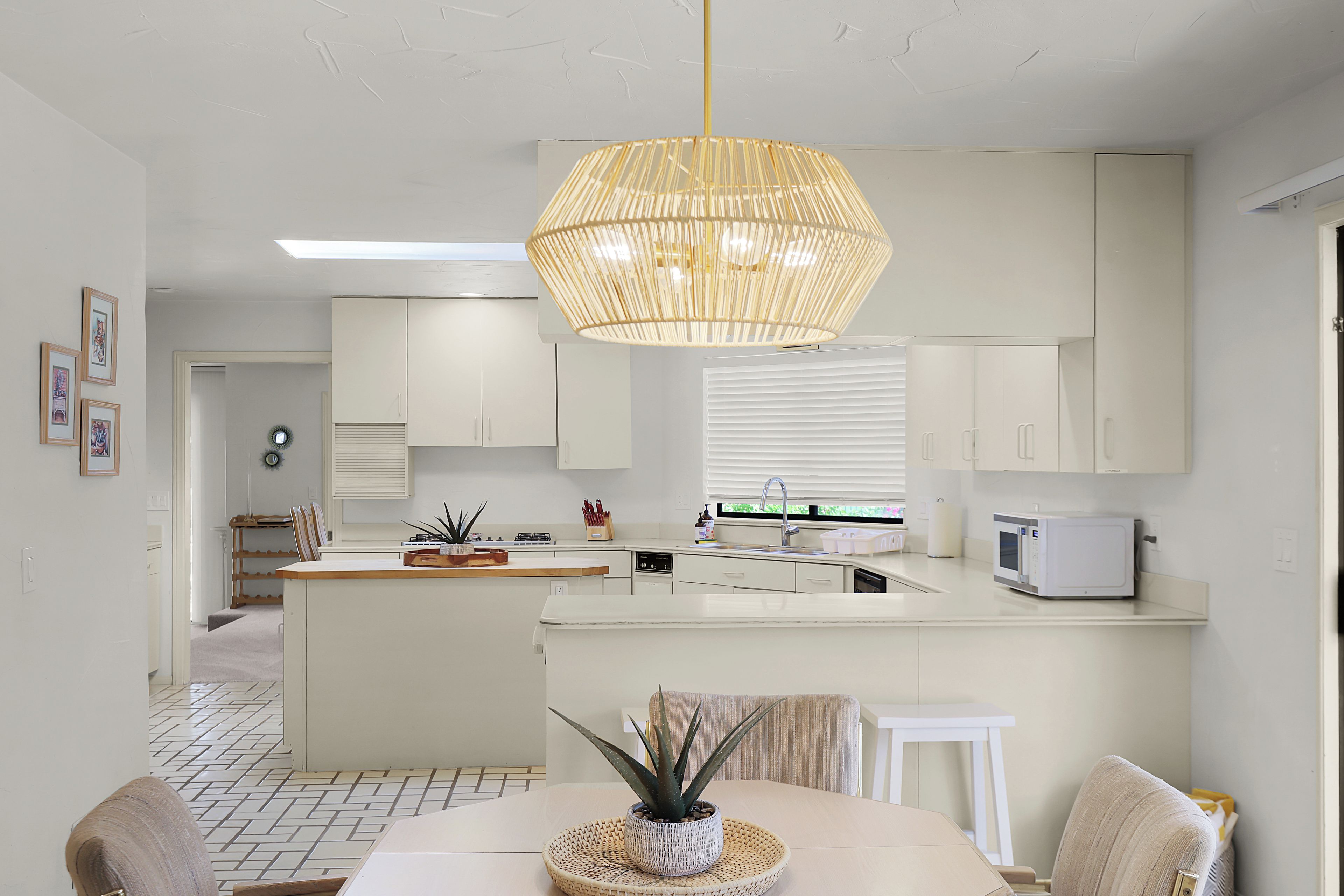 Une cuisine moderne avec des meubles blancs, un îlot central et un luminaire suspendu.
