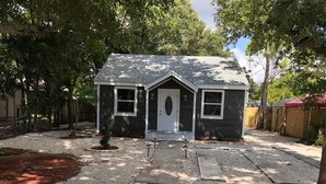 A small, single-story house with a front porch, a garage, and a backyard with a wooden fence.
