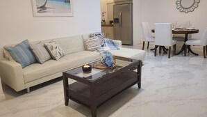 A living room with a beige sofa, a coffee table, and a dining area with a table and chairs.