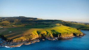 A coastal landscape with rolling hills, a clear sky, and a view of the sea. - Harbourside Studio Apartment (Kiama)