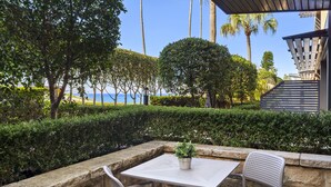 Uma área externa com mesas e cadeiras, um vaso de planta e vista para o mar.