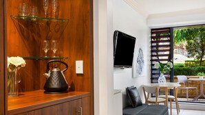 A modern living room with a wooden cabinet, glass shelves, a black kettle, and a grey sofa. - Harbourside Studio Apartment (Kiama)