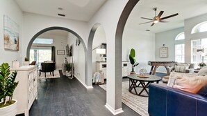 Un amplio espacio de sala con piso de madera oscura, un sofá azul y un ventilador de techo.