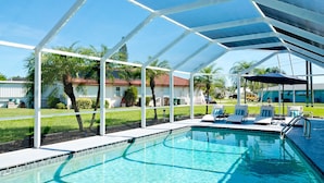Un área de piscina con terraza techada, sillas de descanso y una piscina azul cristalina.