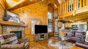 Ein Interieur einer Blockhütte mit Kamin, Fernseher, Holzmöbeln und Küchenzeile.