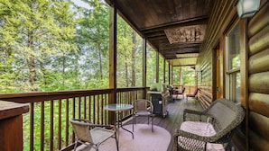 Eine Holzterrasse mit Korbmöbeln und Grill, mit Blick auf einen Wald.